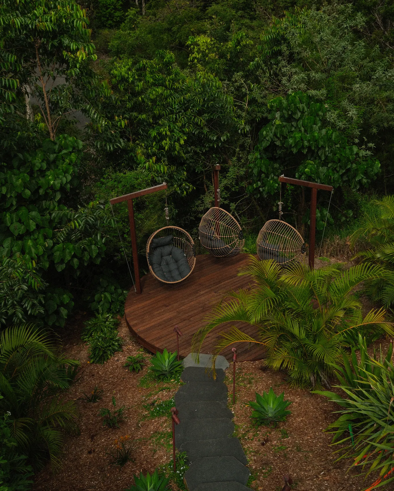 A round timber deck and hanging chairs cut into a rainforest slope
