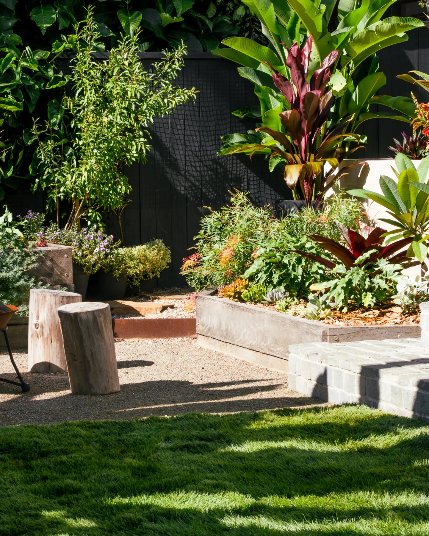 Raised garden beds planted out, with timber stump seats on a strip of lawn